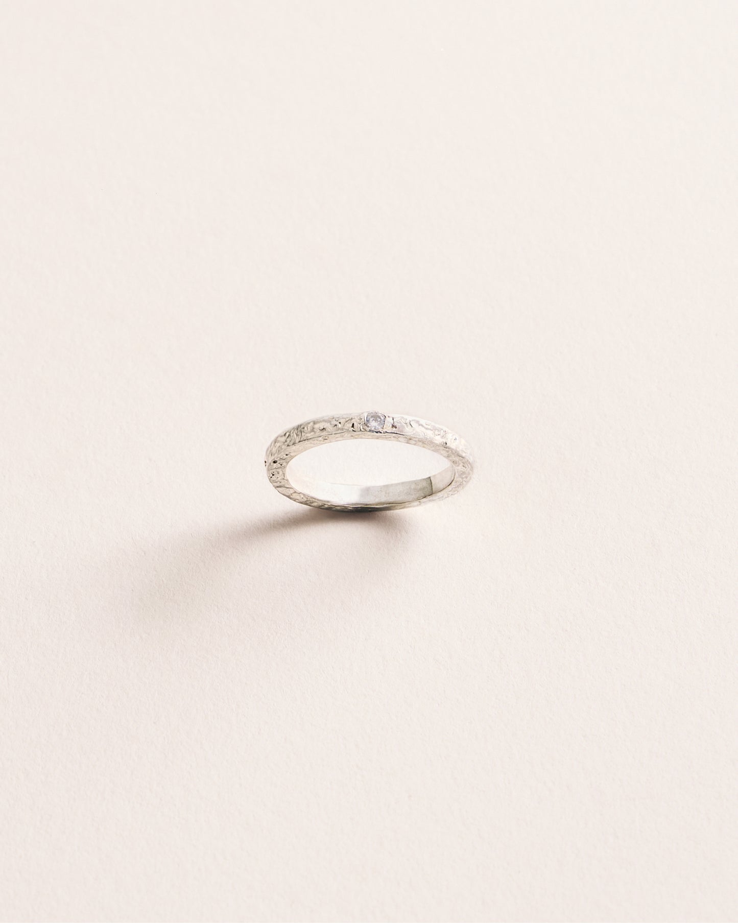 Silver ring with small diamonds on a light beige background