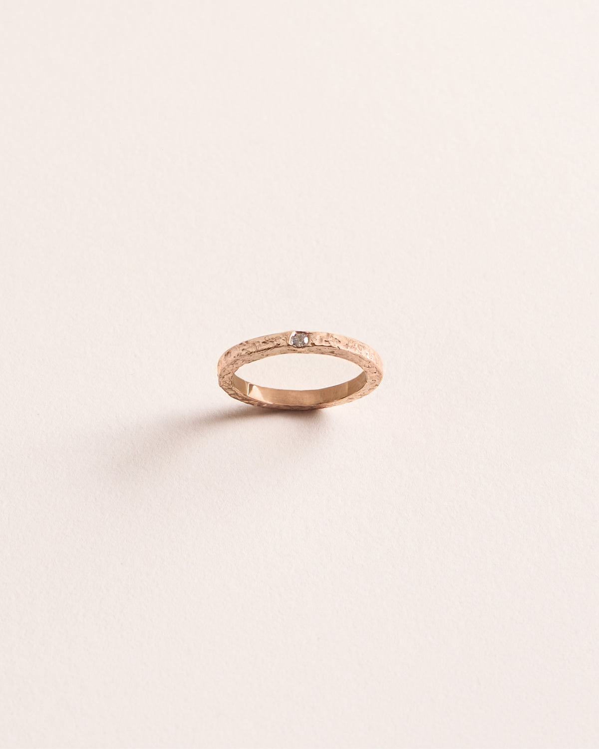 Rose gold ring with a small diamond on a light pink background